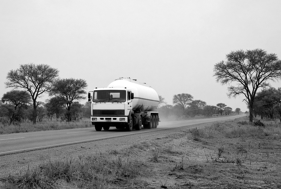 A tanker travelling along a tarmac road through open scrub.